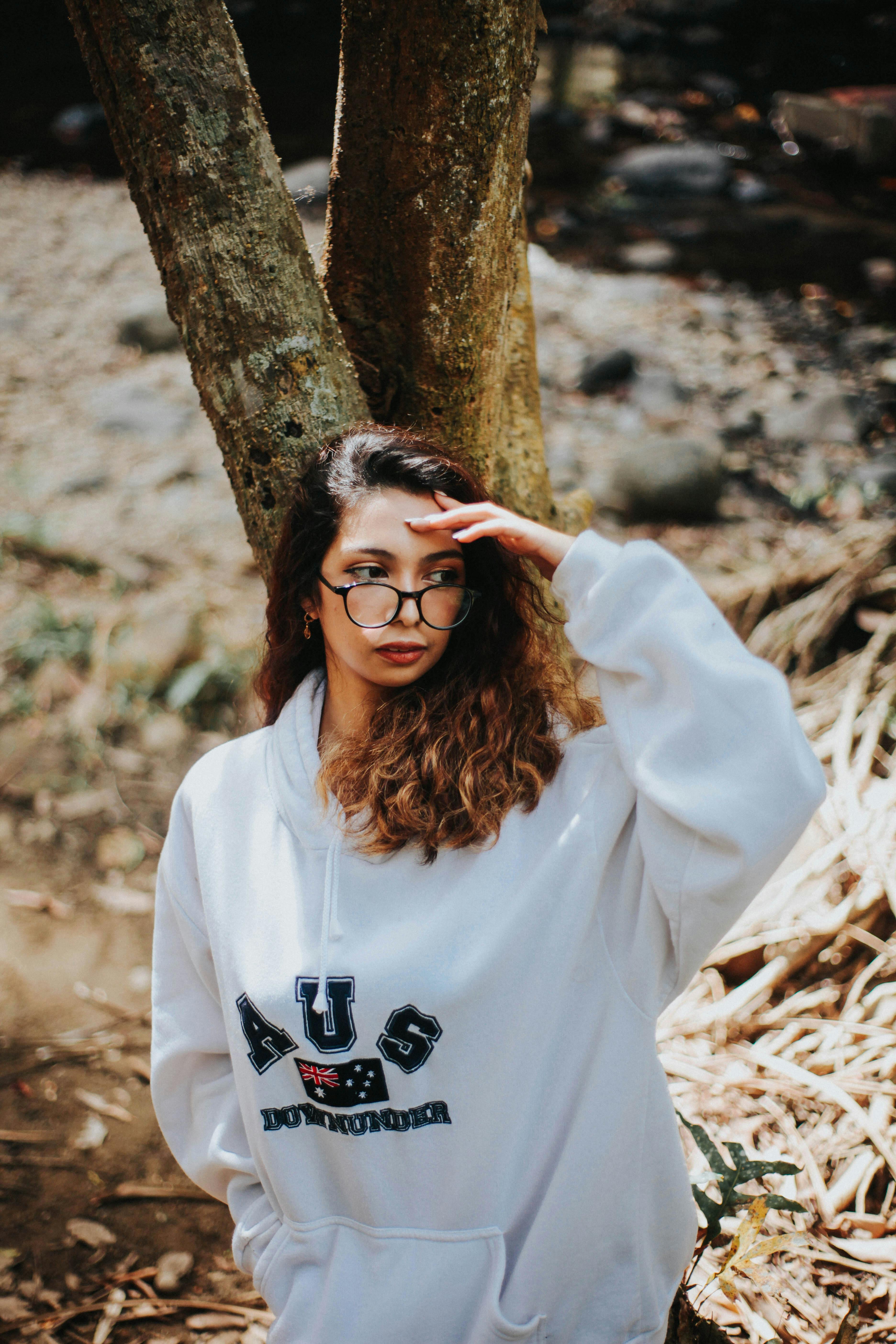 明亮的日光下，一位时尚的年轻女子戴着眼镜，站在户外的自然环境中