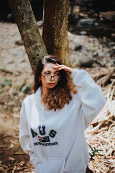 明亮的日光下，一位时尚的年轻女子戴着眼镜，站在户外的自然环境中