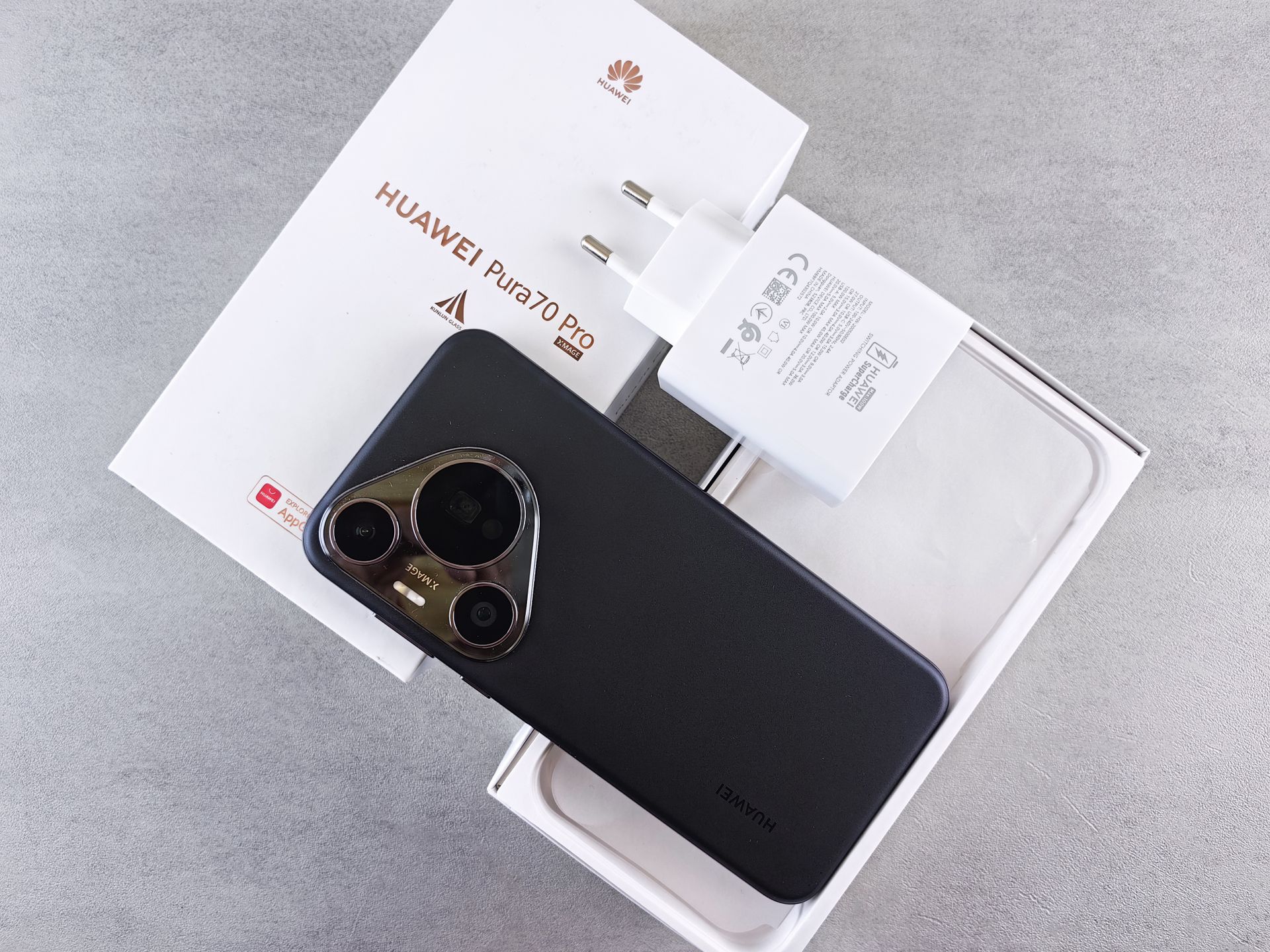 Flat lay of HUAWEI P70 Pro box, phone, and charger on gray surface.
