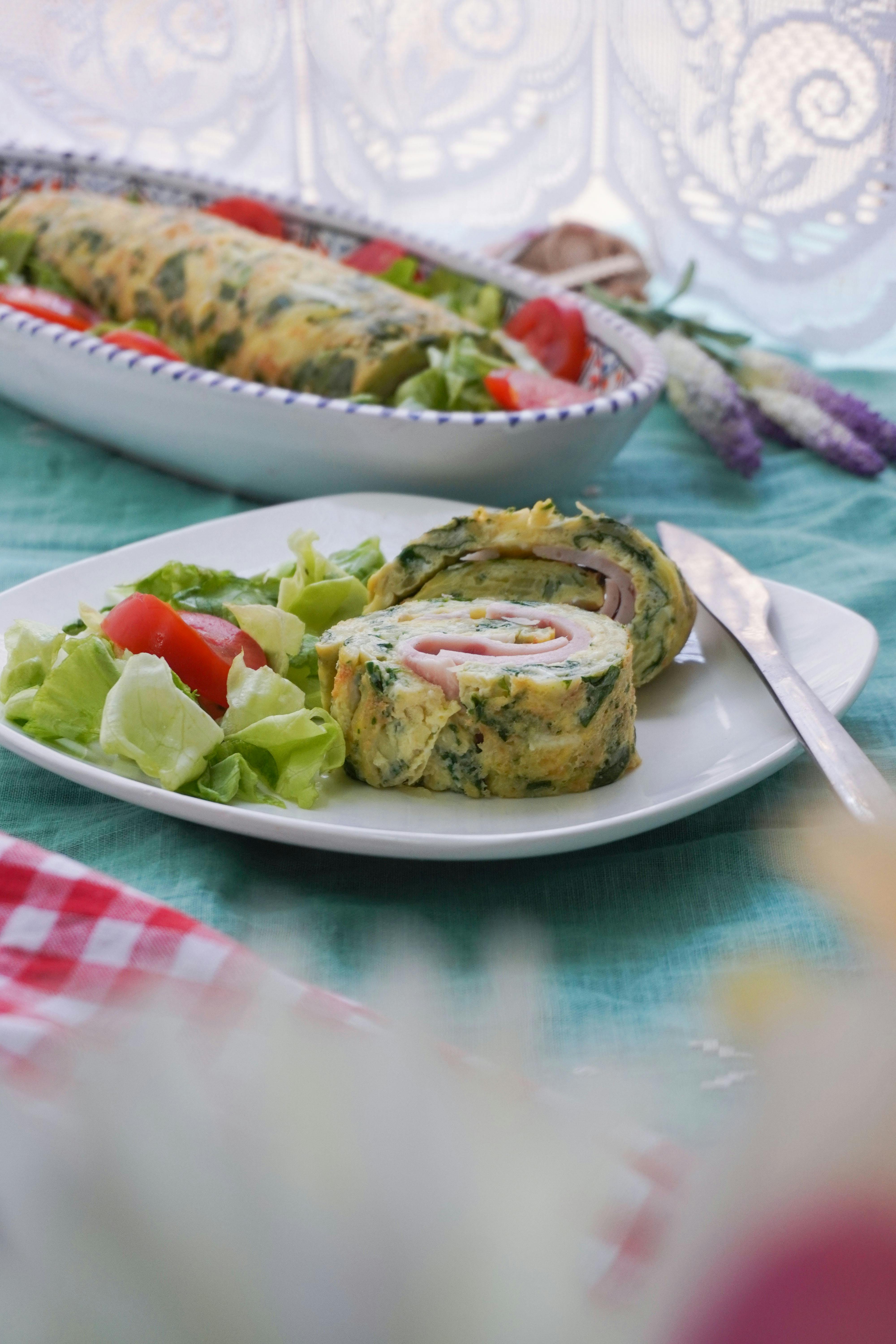 A savory herb omelette roll served with a fresh lettuce and tomato salad on a white plate.