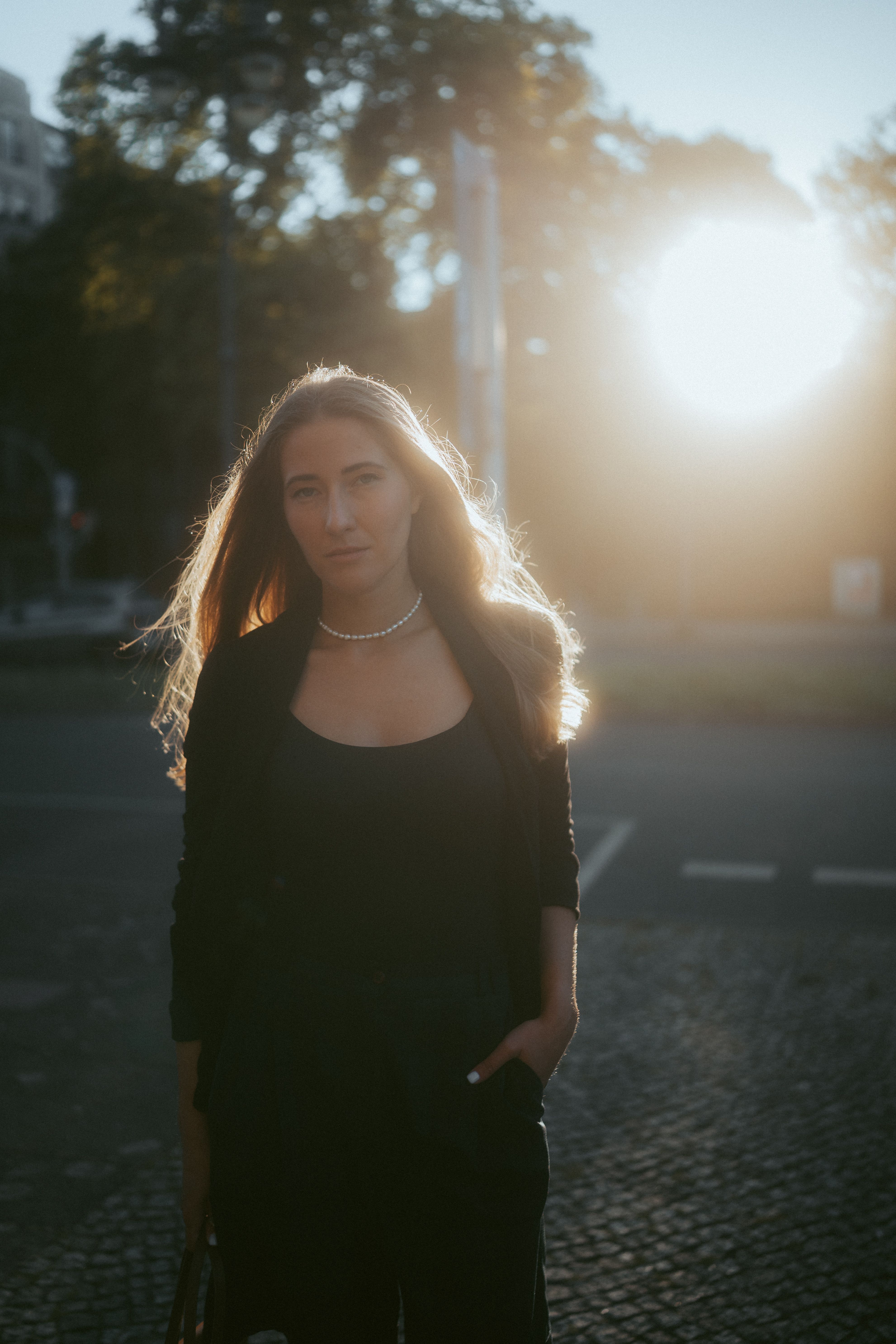 A young woman stands against a backlit sunset in Berlin, creating a dramatic silhouette effect.