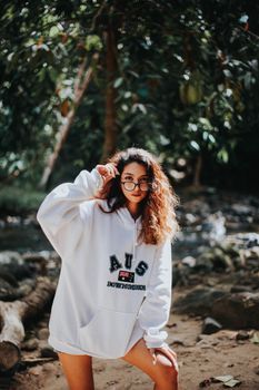 一名年轻女子身穿白色连帽衫，在河边户外摆出休闲时尚的姿势