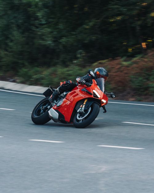 Free Red motorcycle racing on a winding road with blurred motion and forest backdrop. Stock Photo