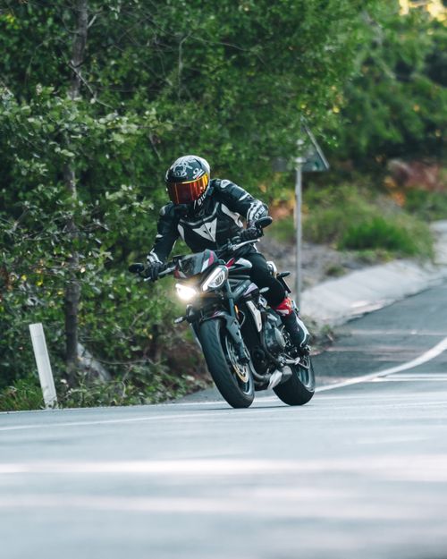 Free Motorcyclist in full gear rides through a scenic winding forest road, capturing the thrill of adventure. Stock Photo