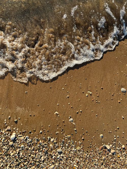Free Gentle ocean waves caress a sandy beach, revealing pebbles in a serene coastal scene. Stock Photo