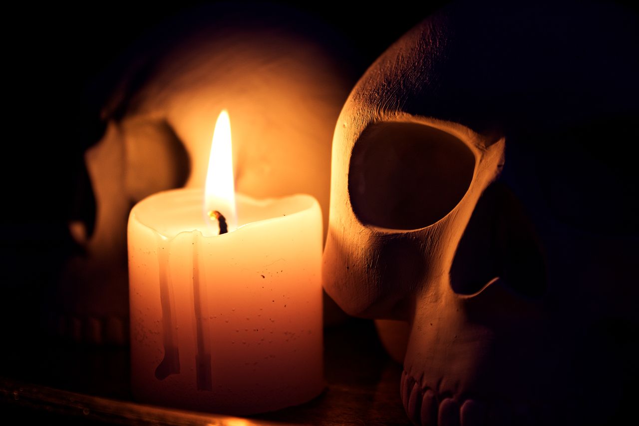 a dramatic still life featuring a candle illuminating two human skulls