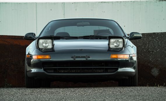 A vintage sports car featuring pop-up headlights viewed from the front against an urban backdrop.