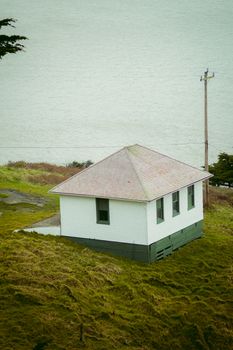 A lone white house perched on grassy terrain with an ocean backdrop, exuding tranquility. — photo by RITESH SINGH