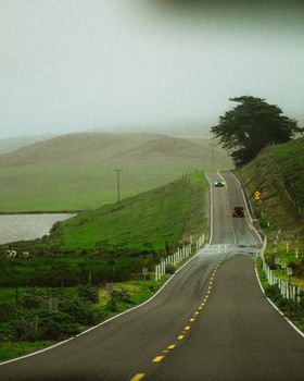Winding rural road through lush green hills in foggy weather, ideal for travel and adventure themes.