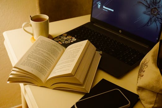 Open book beside a laptop and cup of tea on a desk, perfect for study or work from home.