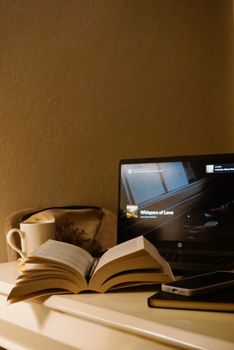 Warm ambient lighting over an open book, laptop, and coffee cup creating a cozy reading workspace.