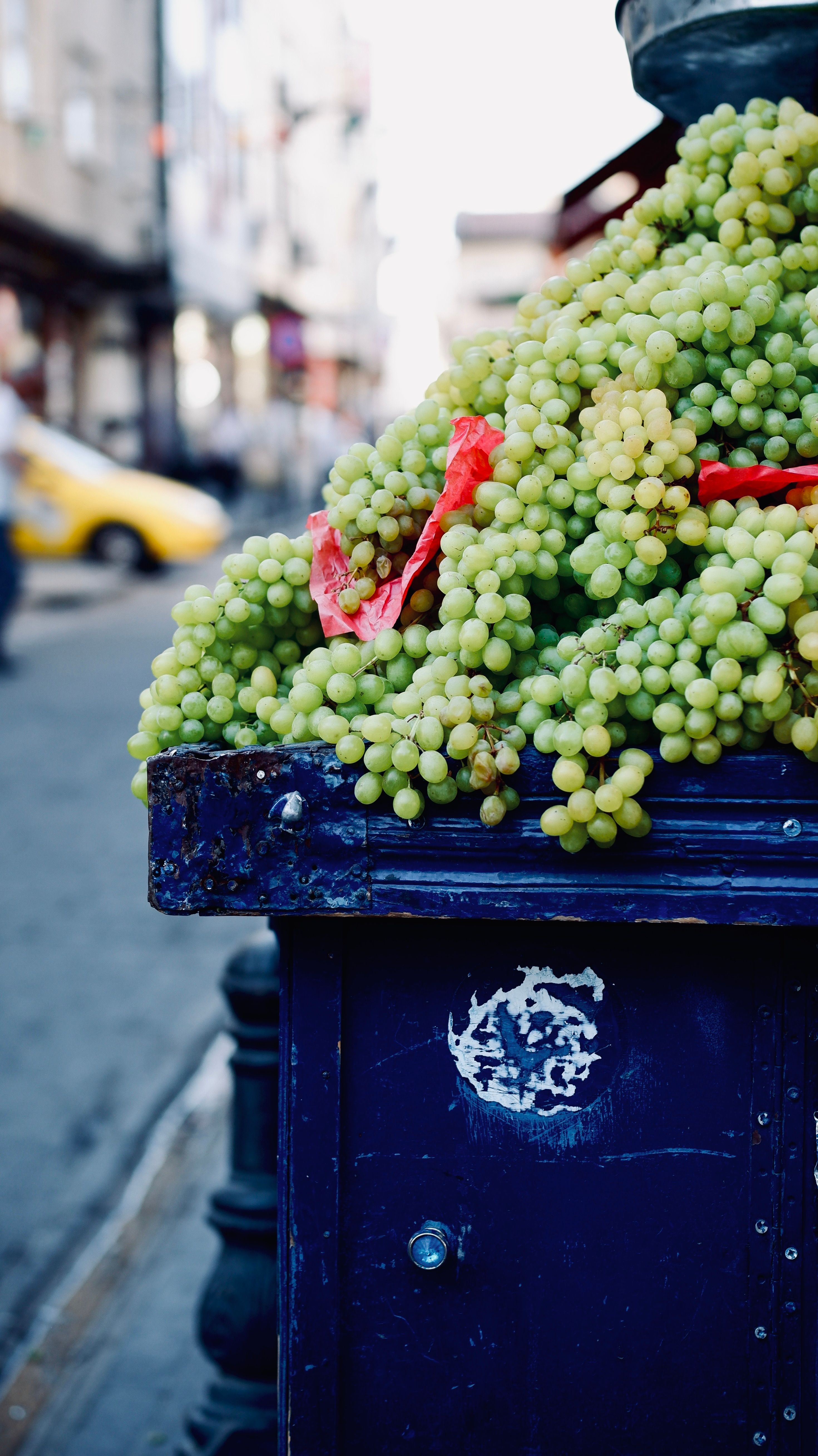 Overflowing bunches of green grapes on a rustic street stall, city background blurred.