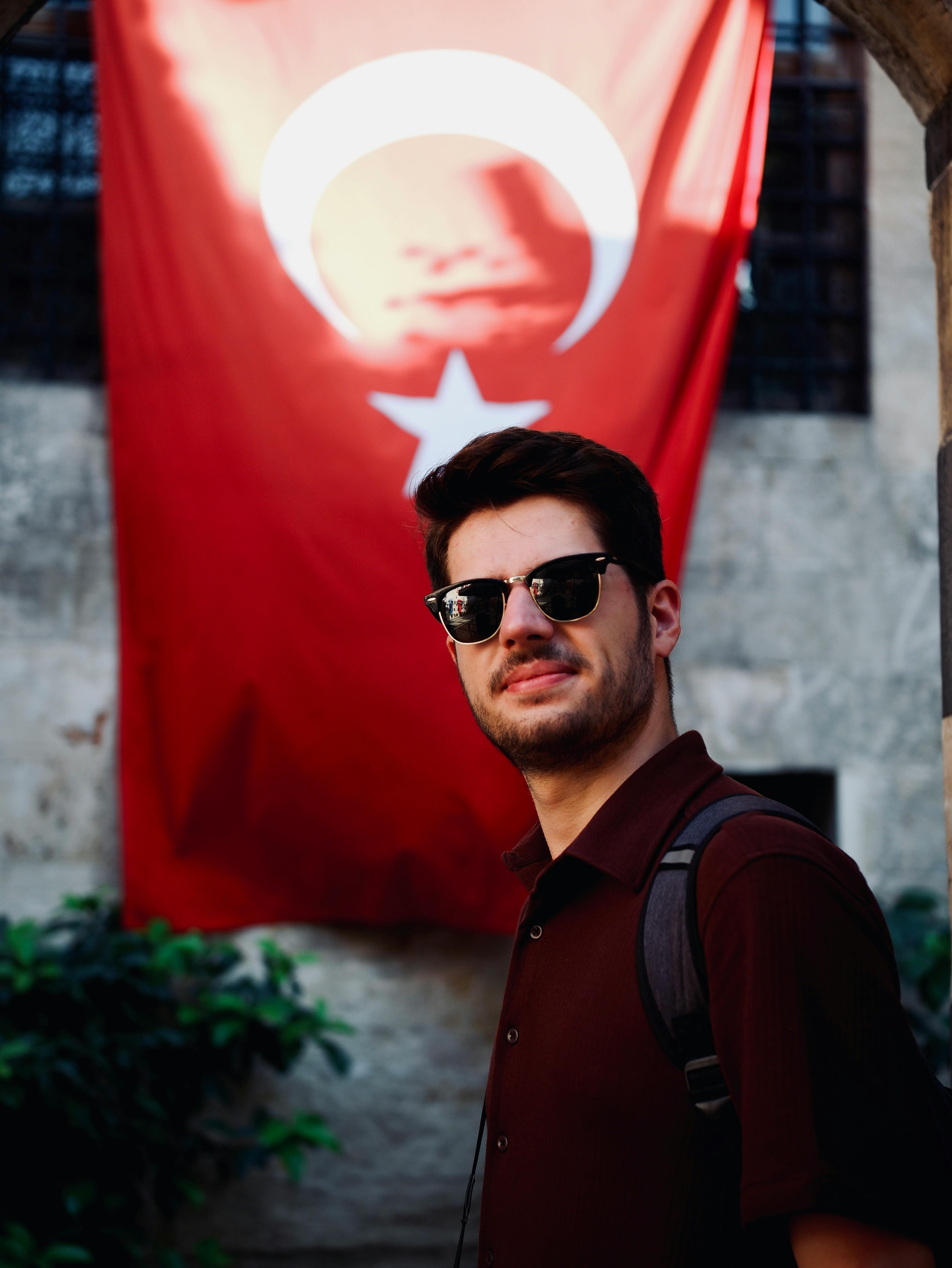 Man in sunglasses standing in front of Turkish flag outdoors, Istanbul.