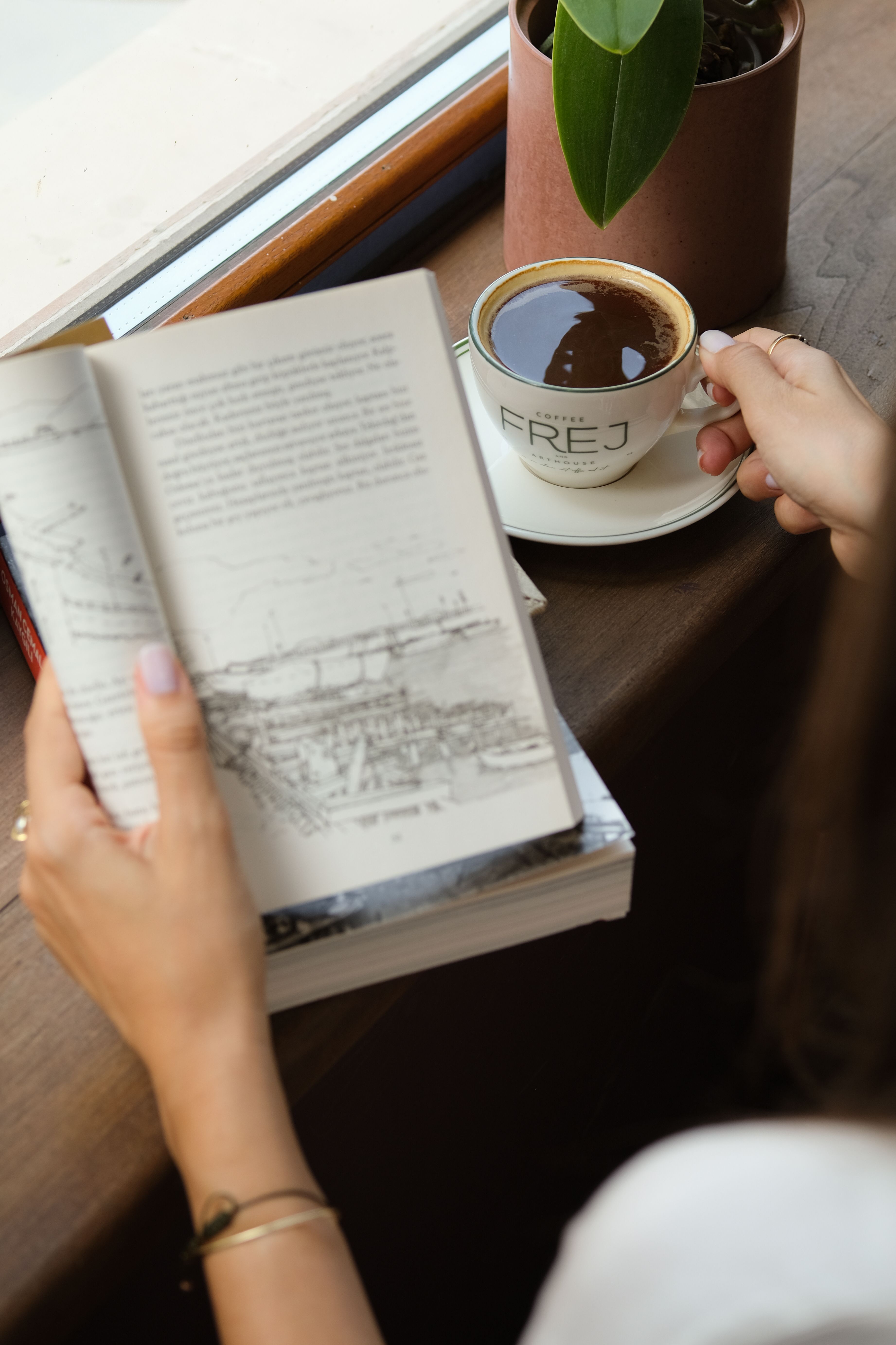 Person reading a book beside window with a cup of coffee in İstanbul café.