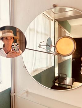 Artistic mirror selfie with hat and vibrant lighting in beautifully designed room.