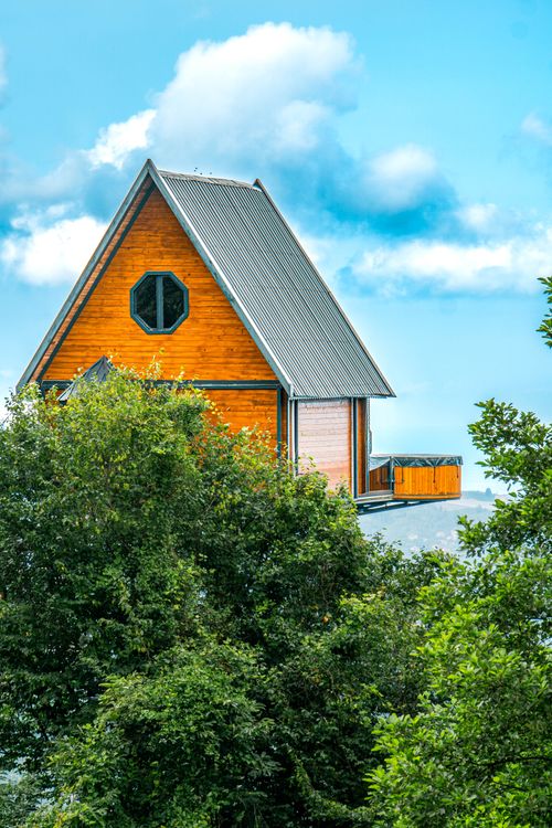 Free A picturesque A-frame cabin surrounded by trees against a blue sky. Stock Photo