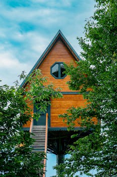 Elevated wooden treehouse nestled among trees with a clear sky backdrop. Perfect for nature retreats.