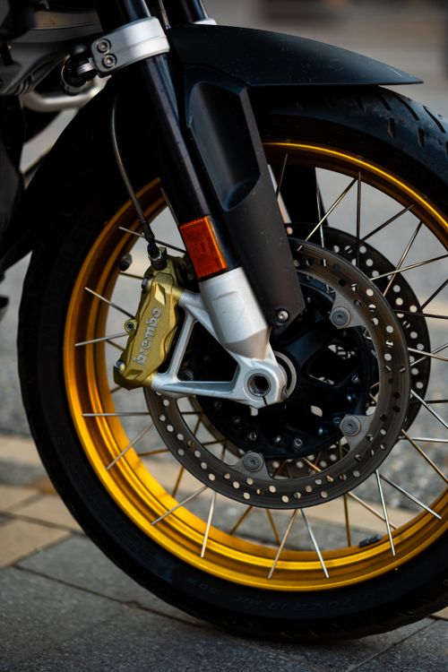 Free Detailed view of a motorcycle front wheel with golden rims and Brembo brake calipers, captured outdoors. Stock Photo