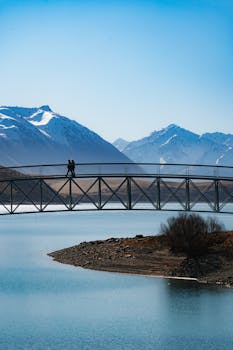 Bridge over calm lake with snow-capped mountains, perfect for travel visuals.