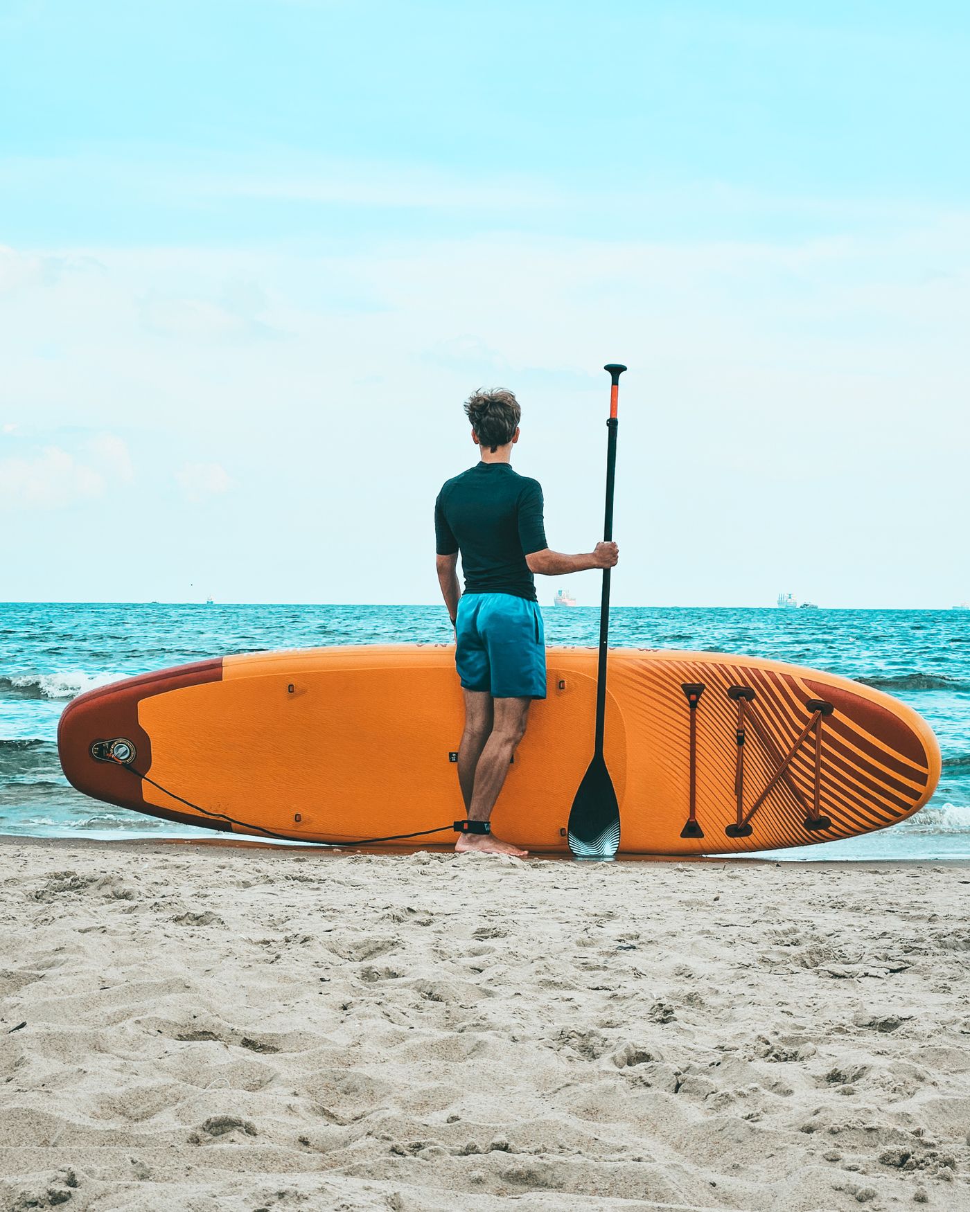 Paddleboarder carrying water-sports equipment along the shore