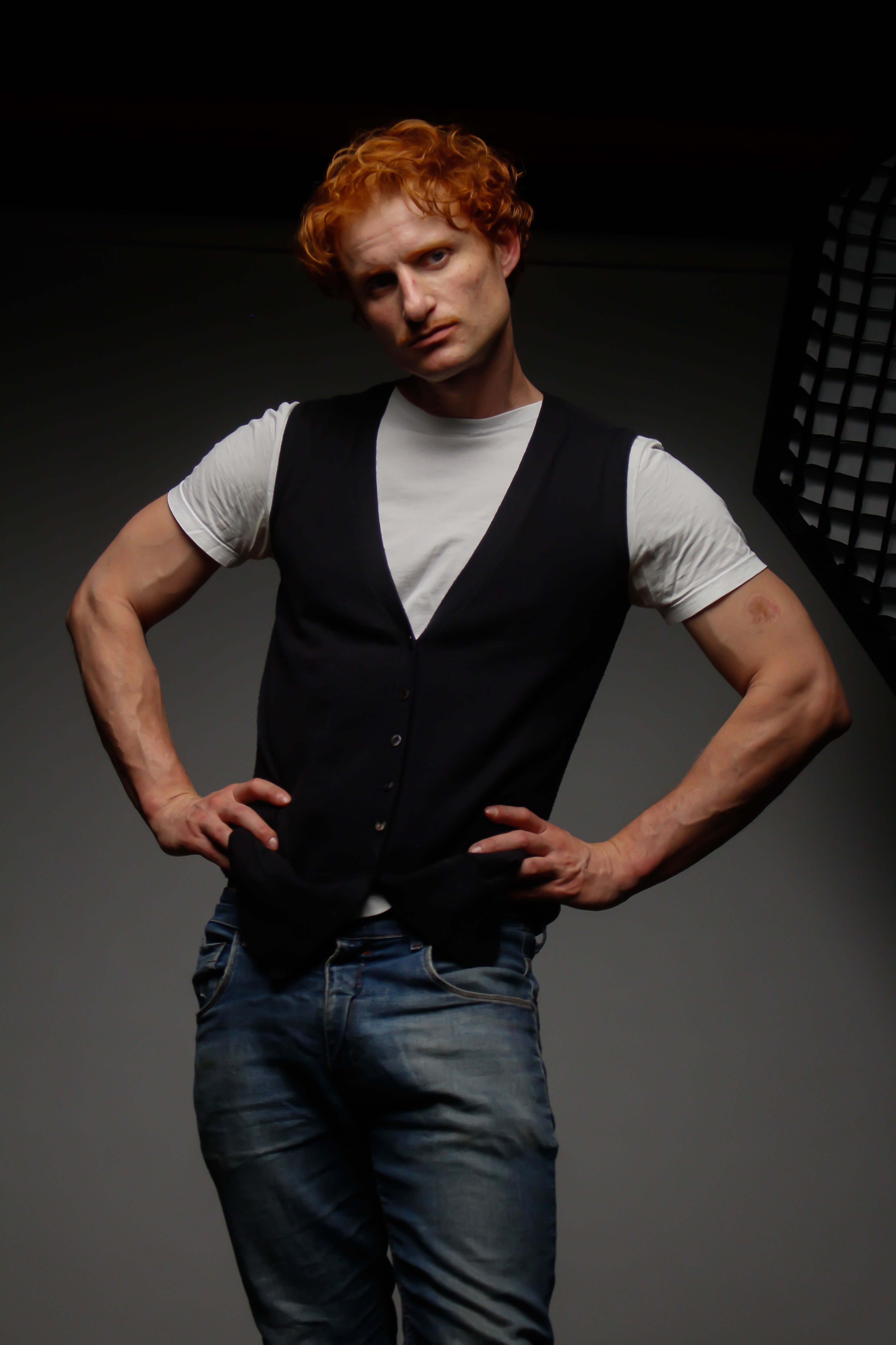 Portrait of a redheaded man in casual attire posing confidently in a studio setting.