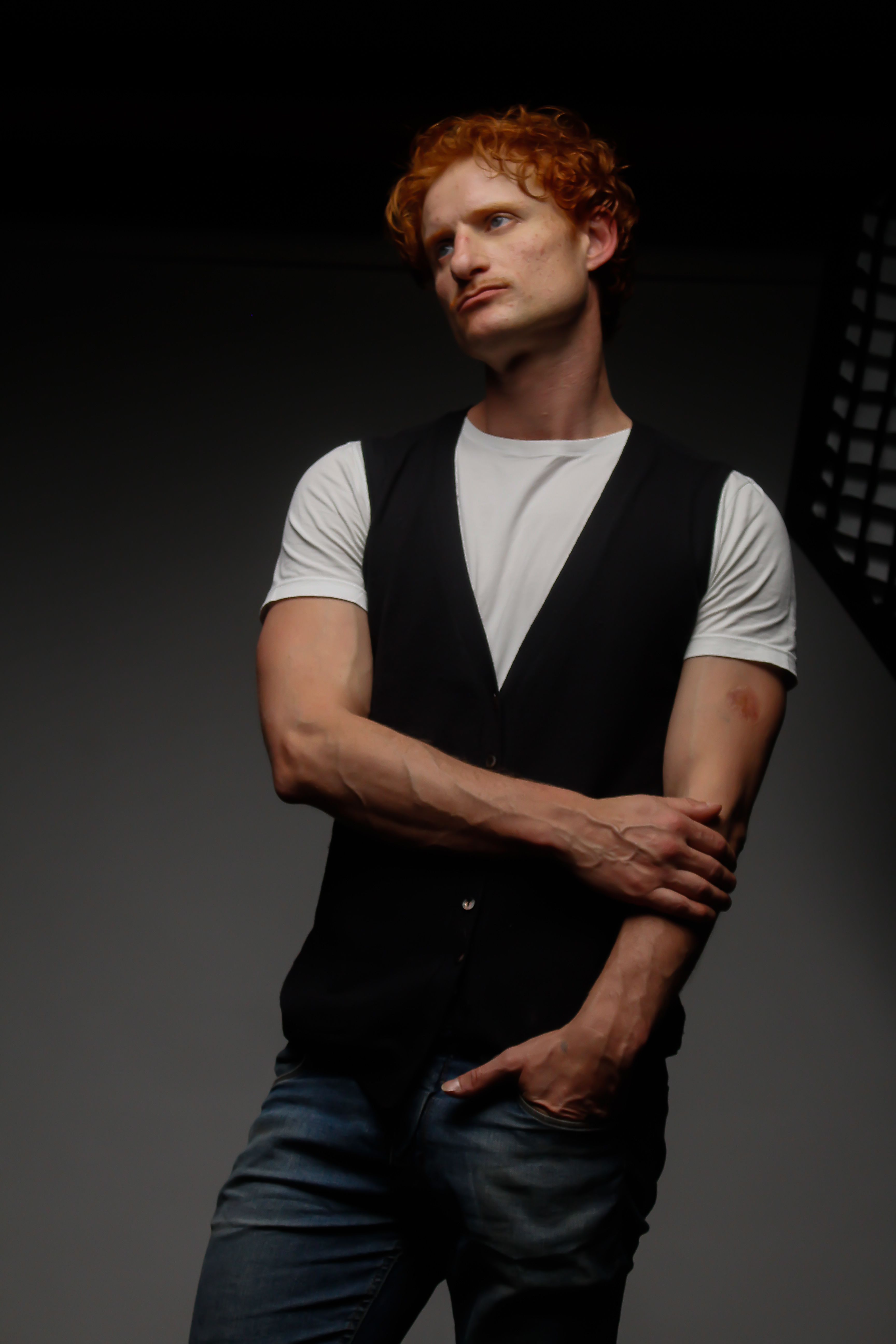 Portrait of a contemplative Caucasian man in a white t-shirt and black vest, posing indoors.