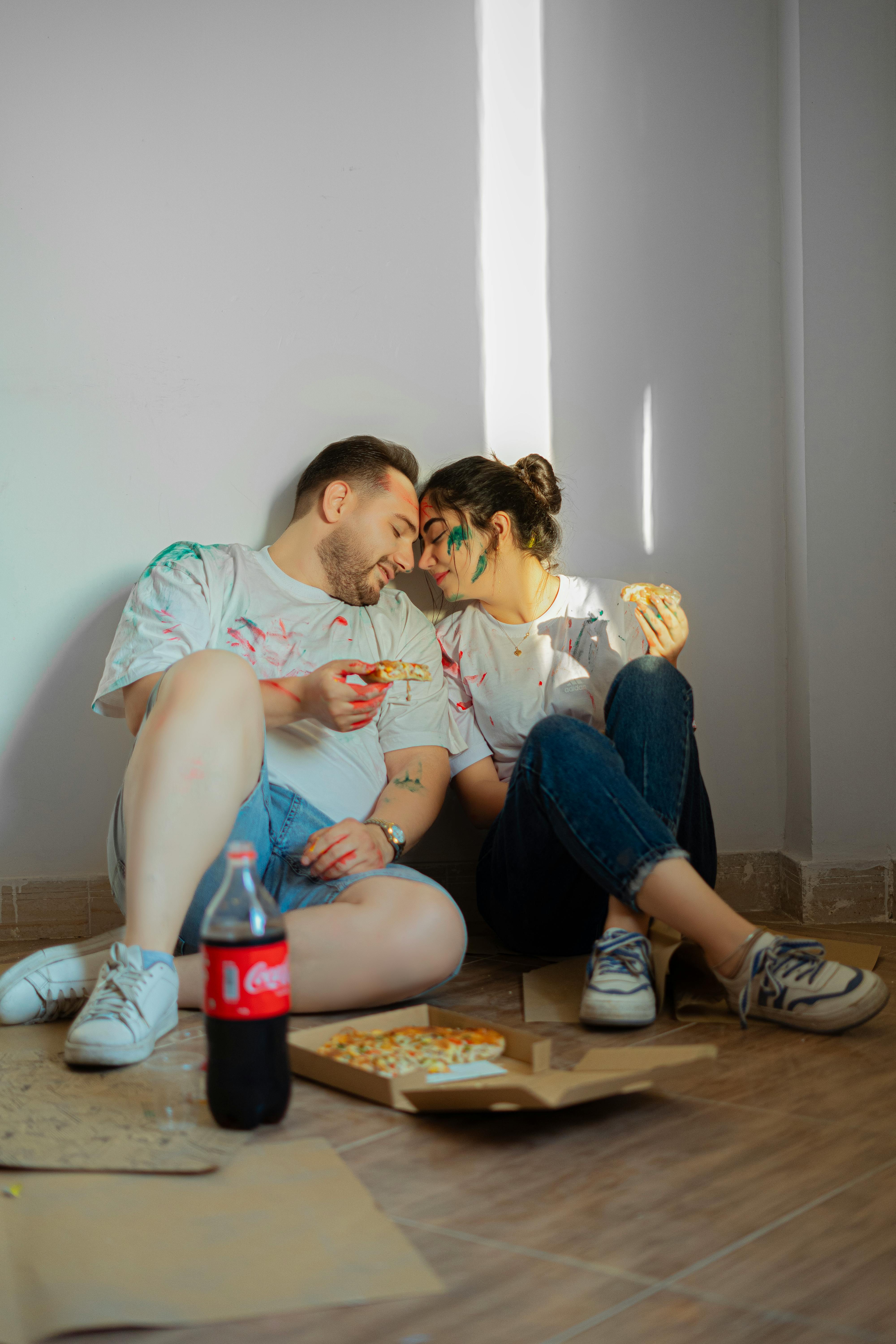 Young couple enjoying a cozy indoor pizza date with Coca-Cola and laughter.