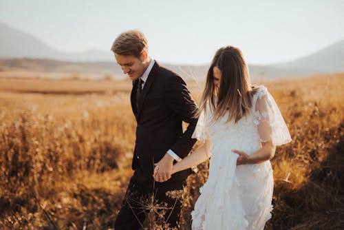 Foto De Foco Raso De Homem Em Terno Formal Preto Segurando A Mão De Uma Mulher Em Vestido Branco