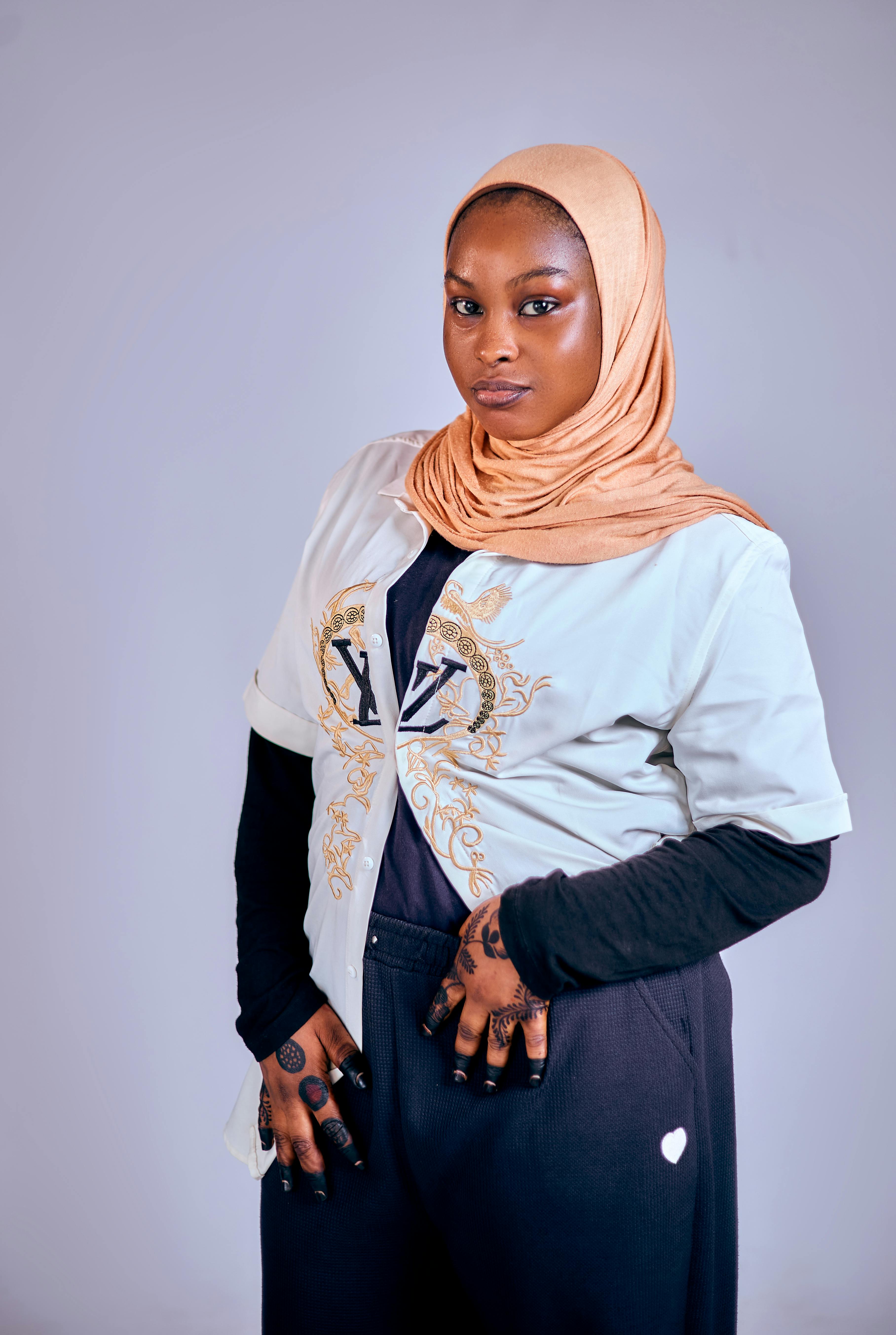 Stylish woman in a hijab showcasing tattoos and modern fashion in a studio setting.