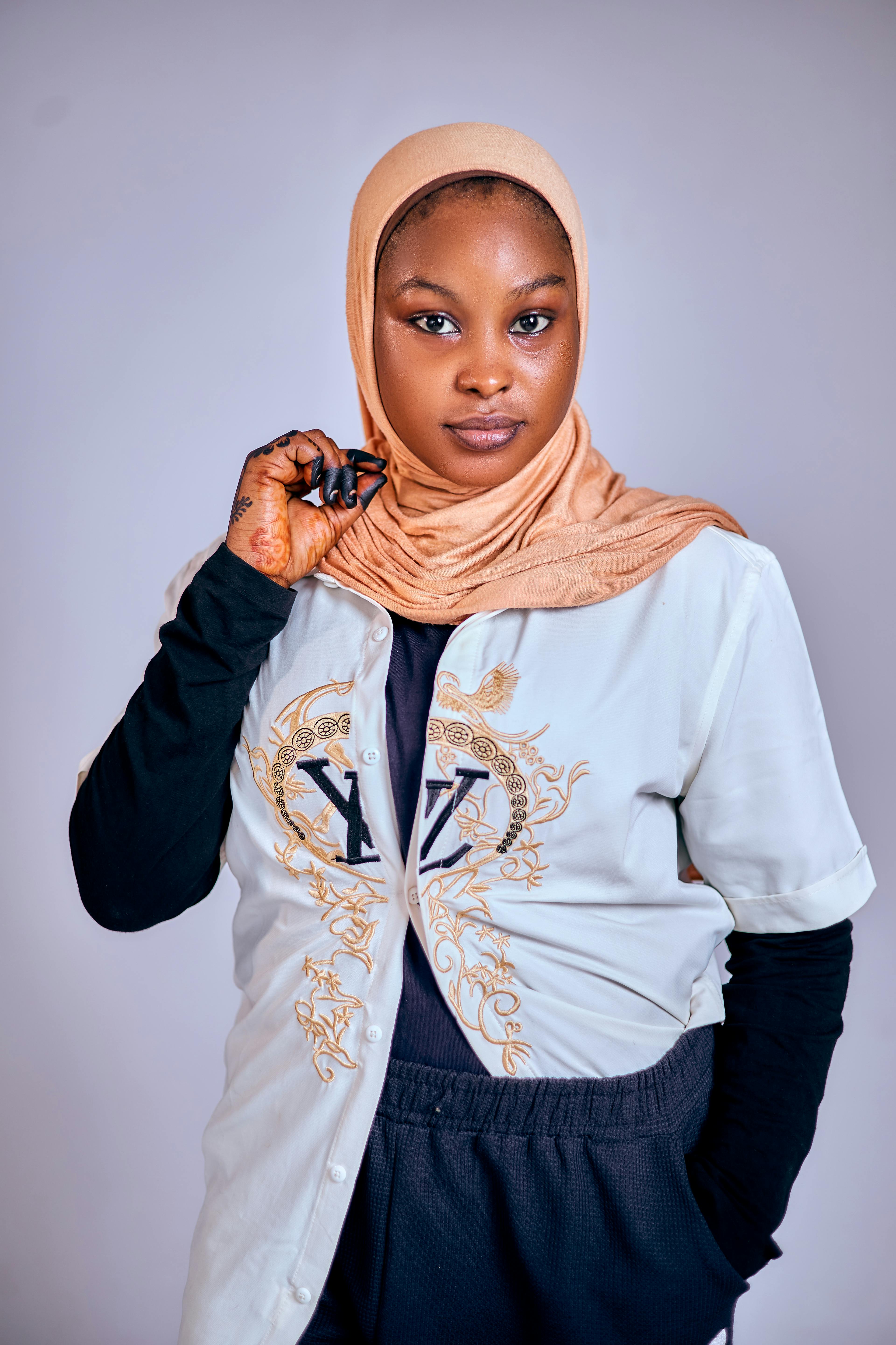 Portrait of a woman in a hijab standing confidently indoors with a neutral background.