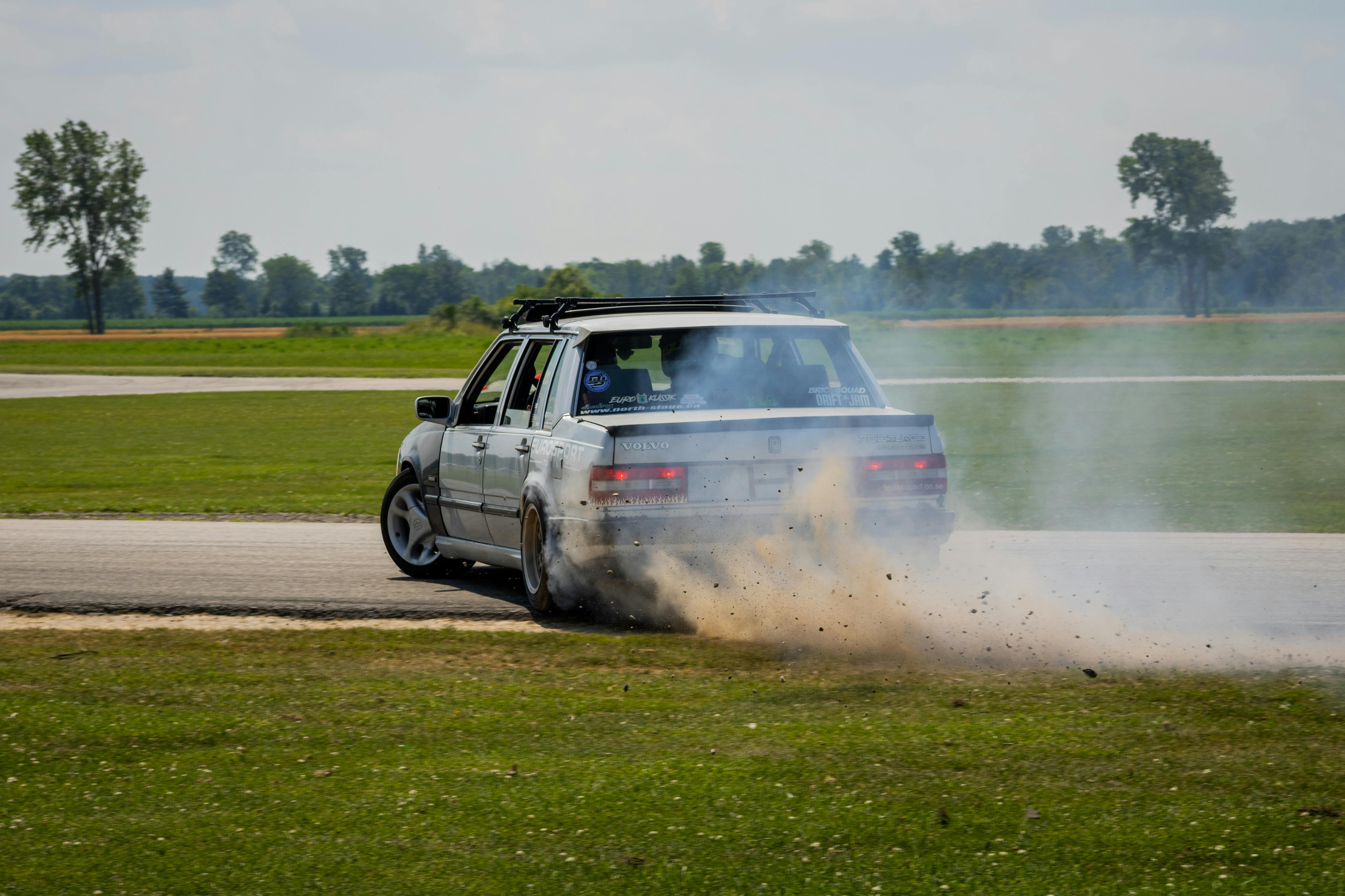 Car performing a dramatic drift on a race track, kicking up smoke and debris.