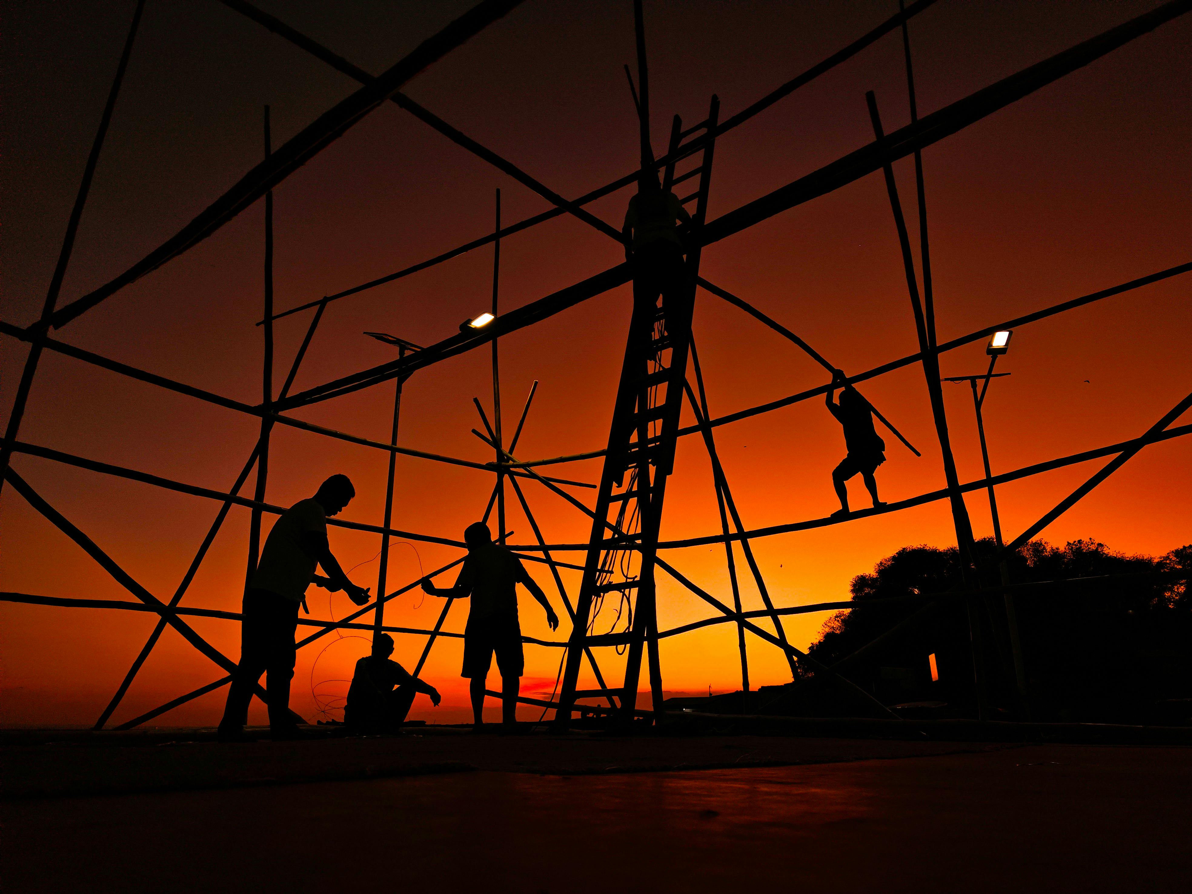 Silhouetted workers constructing bamboo scaffold at stunning sunset.