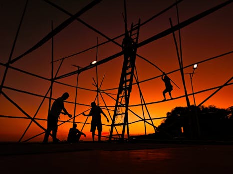 Silhouetted workers constructing bamboo scaffold at stunning sunset.