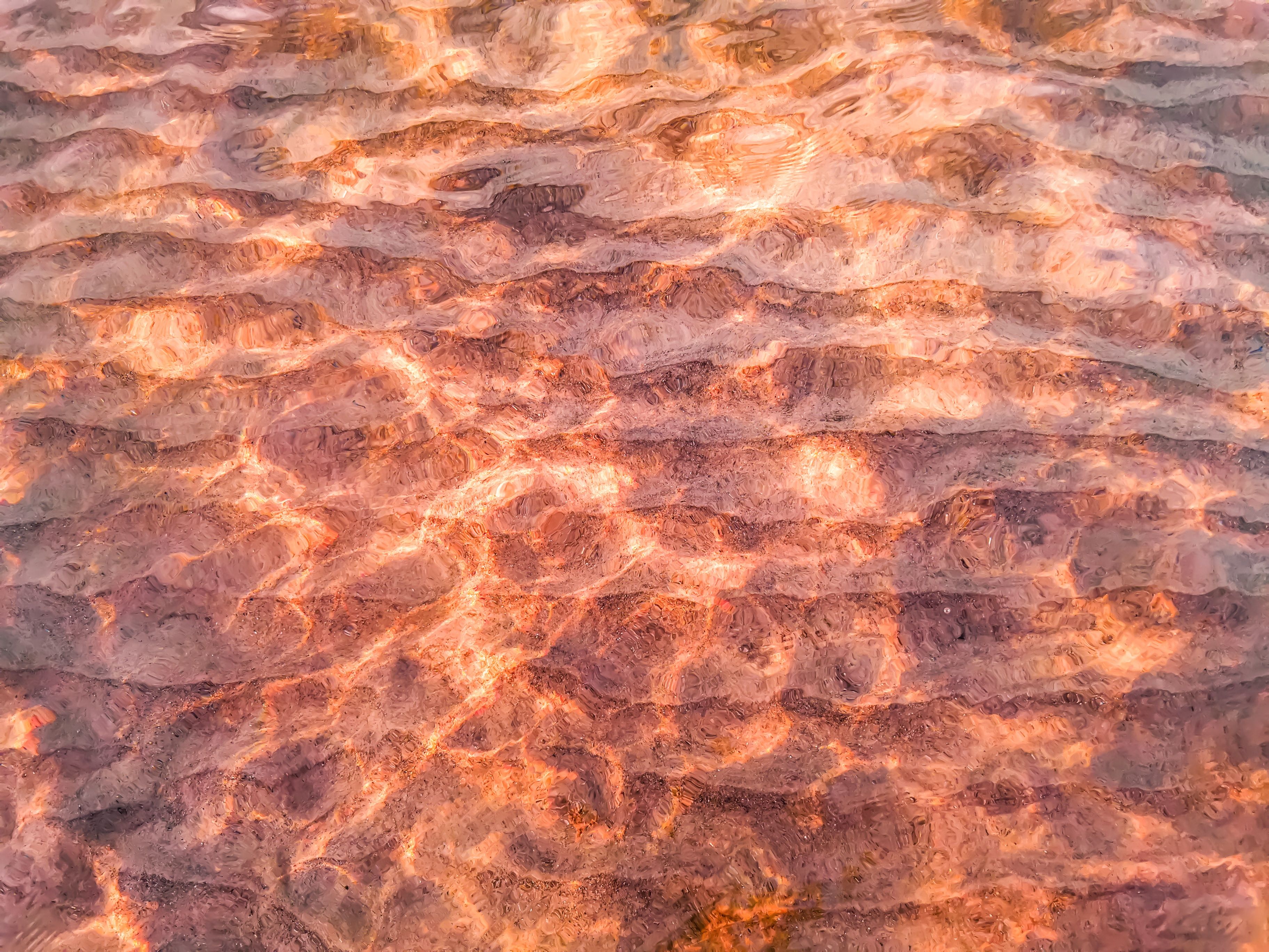 Sunlit ripples creating an abstract, warm pattern on a water surface at sunset.