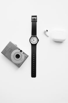 A black and white minimalist setup featuring a watch, camera, and earphones.