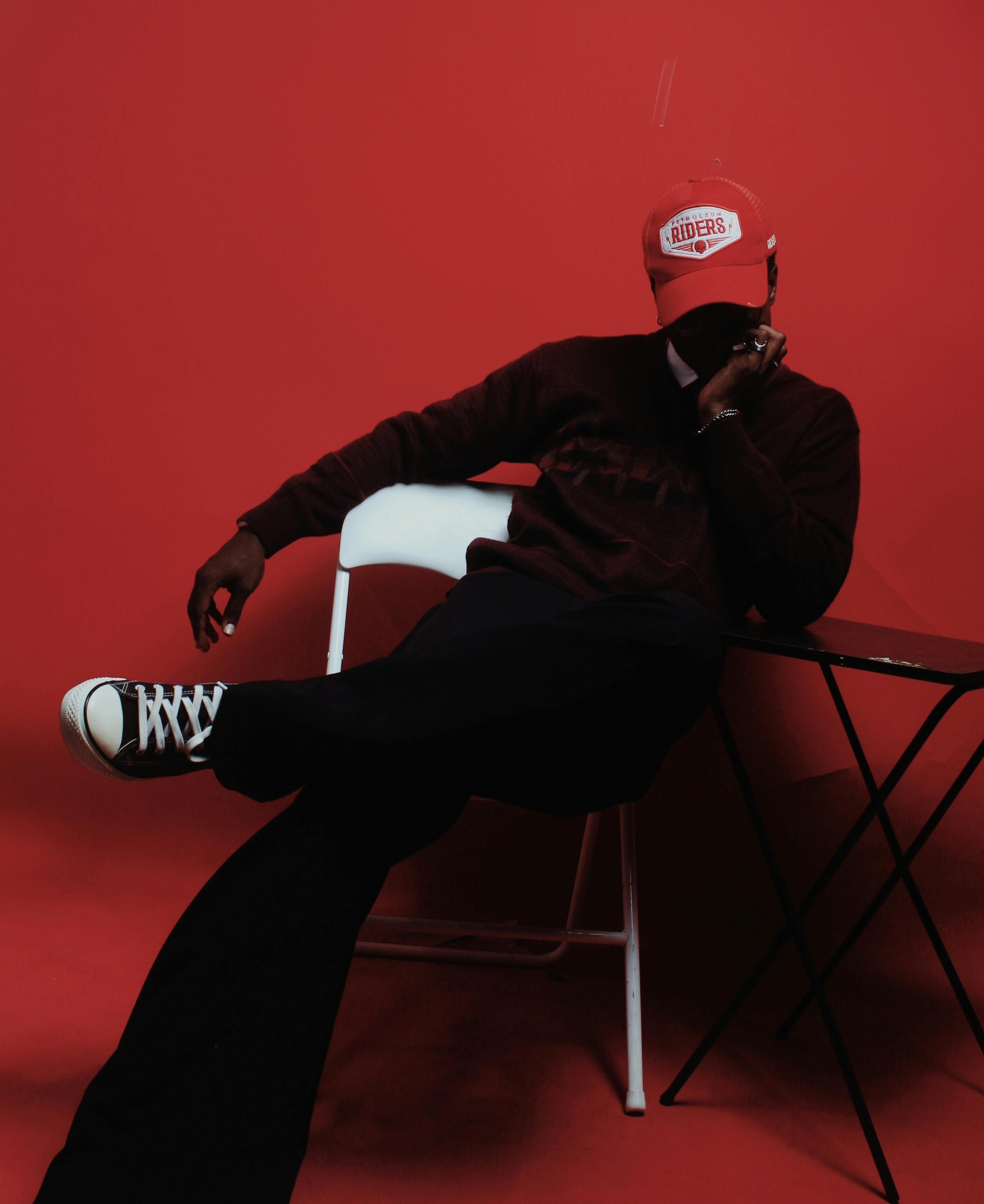 Man posing in a red room wearing a red cap and sneakers, exuding style and modern fashion.