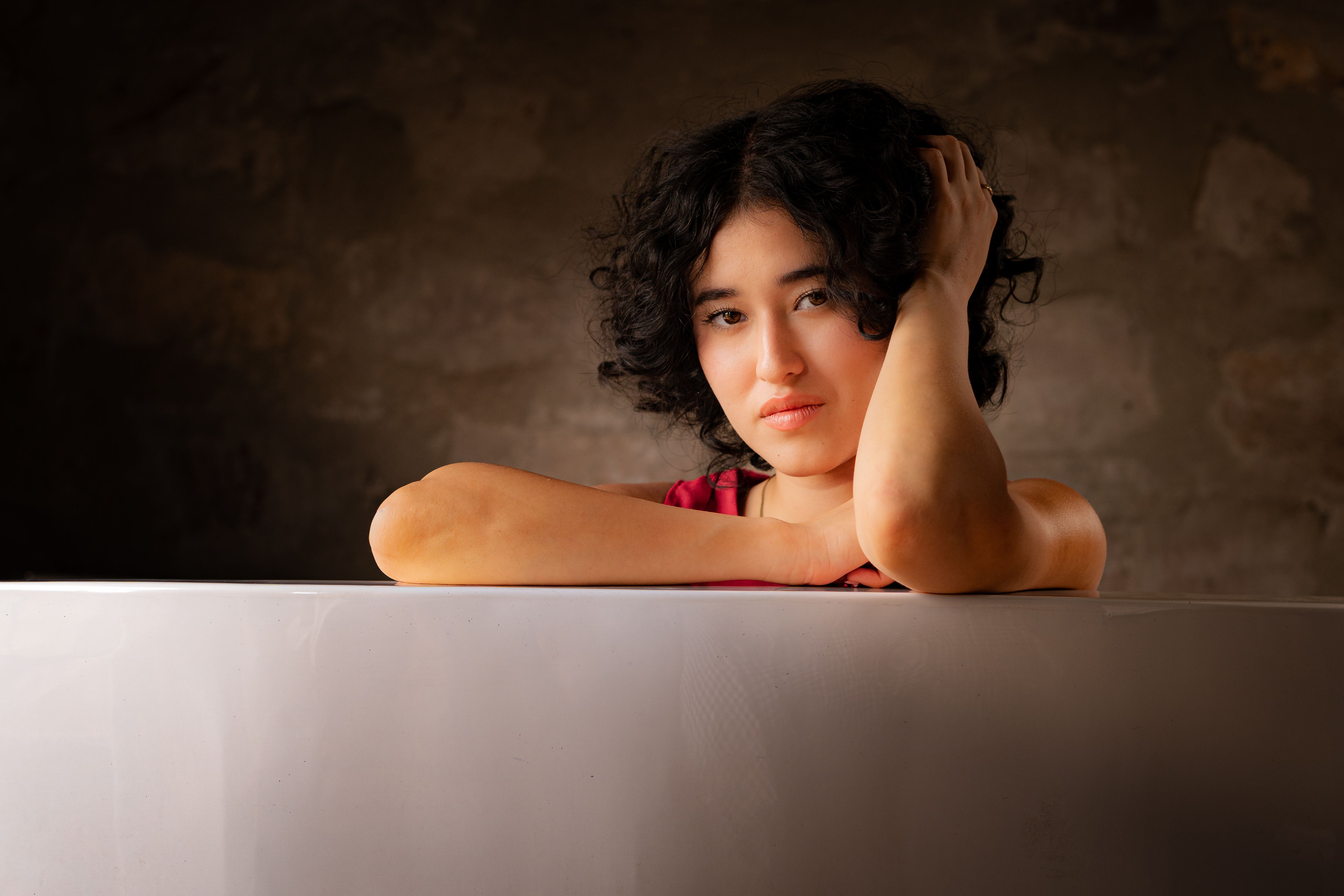 A contemplative woman resting her head on her hand, captured indoors with soft lighting.
