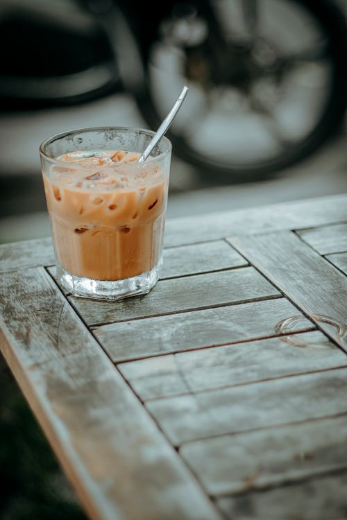 Free A refreshing glass of iced coffee on a weathered wooden table in an outdoor setting. Stock Photo