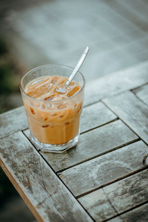 Free A glass of iced coffee with a straw sits on a rustic wooden table outside. Stock Photo
