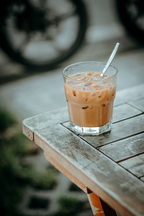 Free Chilled iced coffee with straw on outdoor wooden table, creating a relaxed summer vibe. Stock Photo
