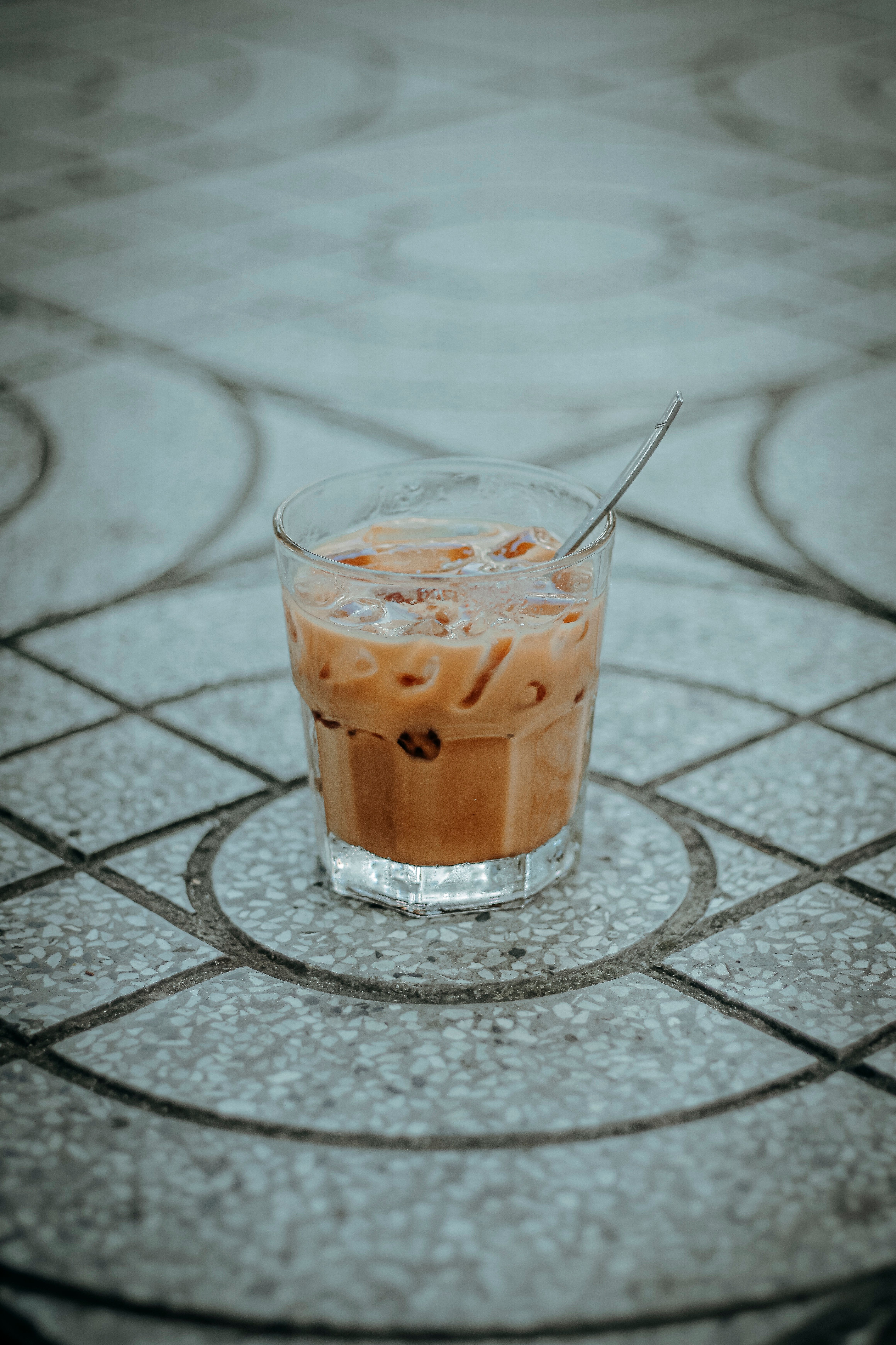 Chilled iced coffee in a glass with spoon, placed on patterned tile. Perfect for summer vibes.