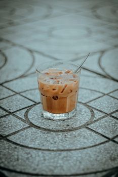 Chilled iced coffee in a glass with spoon, placed on patterned tile. Perfect for summer vibes.