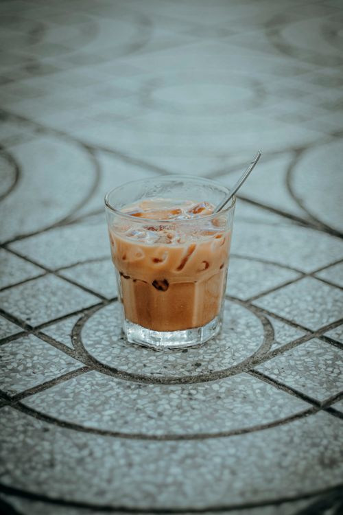 Free Chilled iced coffee in a glass with spoon, placed on patterned tile. Perfect for summer vibes. Stock Photo