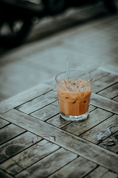 Free A glass of iced coffee with a straw on a rustic wooden table outdoors, creating a relaxed vibe. Stock Photo