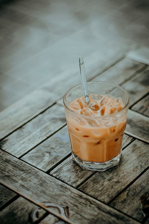 Free Chilled iced coffee glass with straw on a rustic wooden table outdoors. Stock Photo