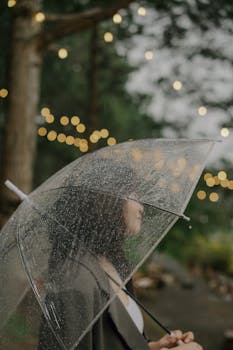 A woman holding a clear umbrella on a rainy day in Đà Lạt, with bokeh lights in the background.
