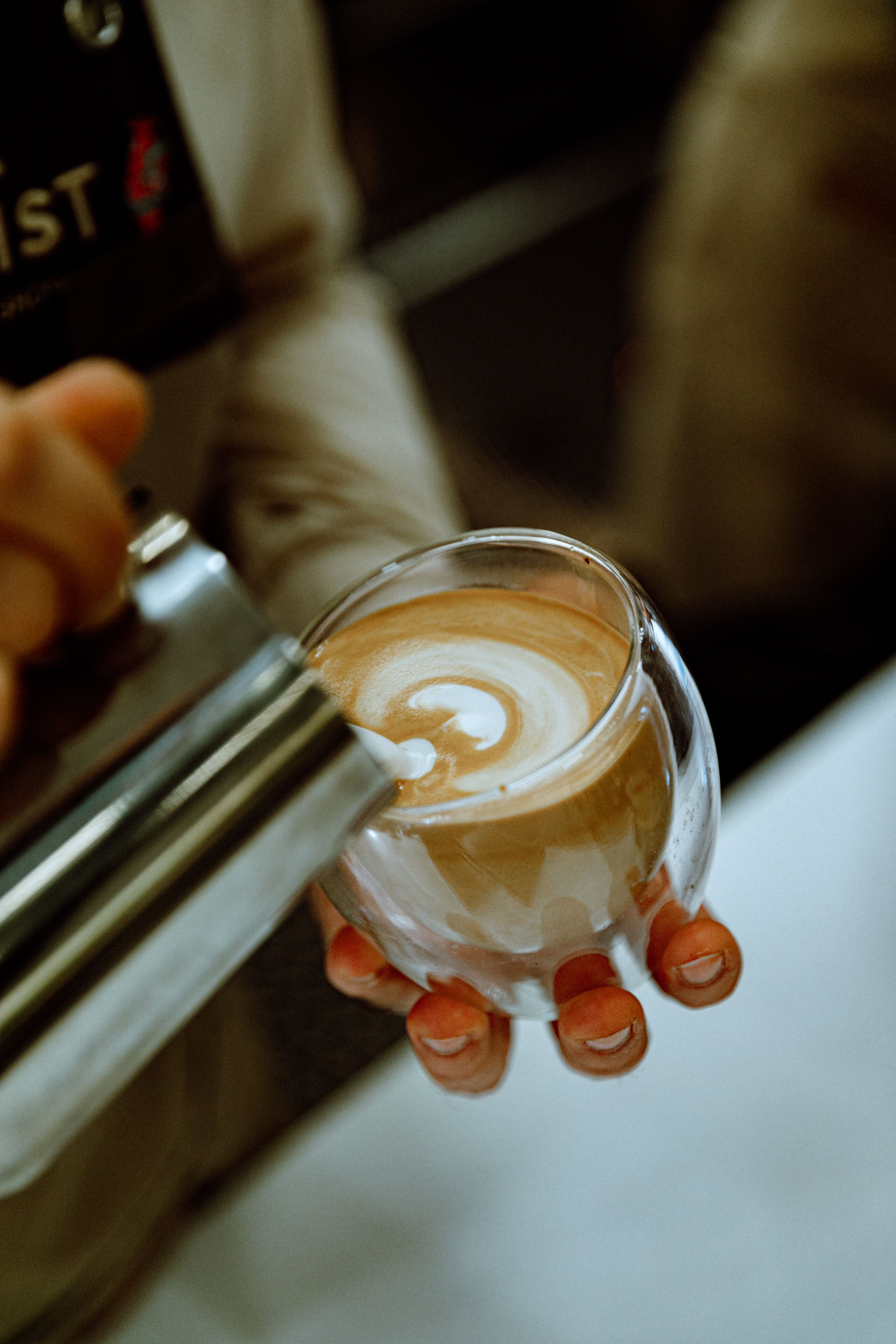 Barista creating intricate latte art in a glass cup at a cozy Baku cafe, showcasing expert coffee craftsmanship.