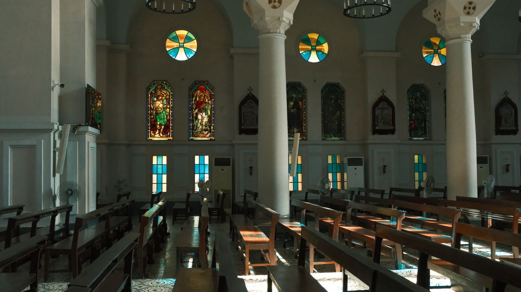 Sunlit church interior with stunning stained glass windows and wooden pews.