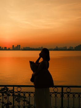 Peaceful silhouette of a woman by West Lake in Hanoi during a vibrant sunset, capturing tranquility.