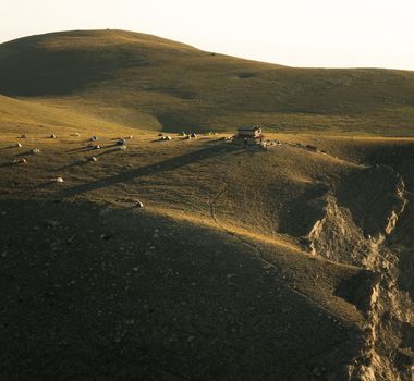Aerial view of tents scattered on a serene mountain plateau bathed in warm light.